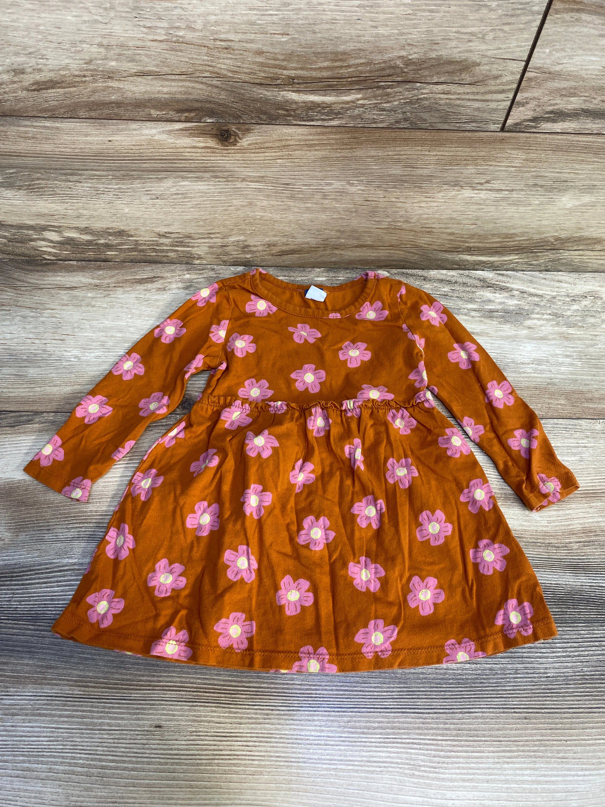 Long sleeve orange toddler dress with pink floral print, laid flat on wood background