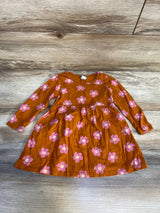 Long sleeve orange toddler dress with pink floral print, laid flat on wood background