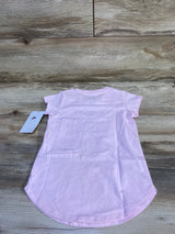 Back view of toddler pink Nike short-sleeve shirt showcasing curved hem and attached Nike tag on a light wood background