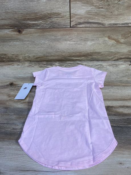 Back view of toddler pink Nike short-sleeve shirt showcasing curved hem and attached Nike tag on a light wood background