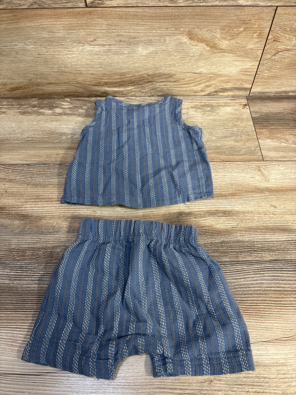 Flat lay of blue striped henley tank and matching elastic-waist shorts, size 6 months, on wood background