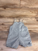 Flat lay front view of toddler denim shortalls showcasing adjustable tan straps, single front patch pocket and rolled hems on wood background