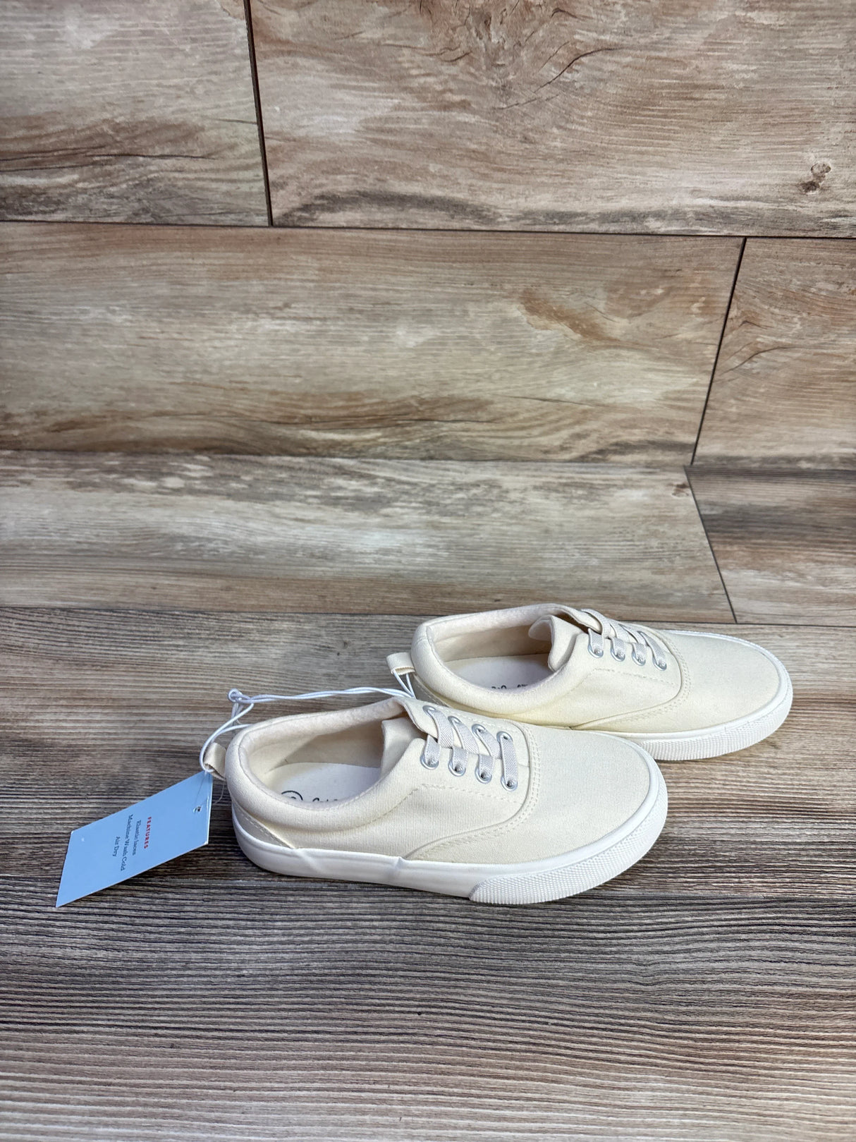 Side view of Cat & Jack Tyler toddler slip-on sneakers in off-white canvas with white rubber sole on wood background