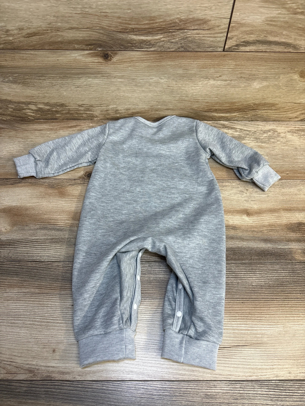 Gray long sleeve baby romper with snap buttons, displayed on wood floor