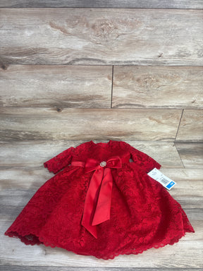 Flat-lay of Rare Editions red toddler lace dress with long sleeves, satin bow and rhinestone brooch on wood floor