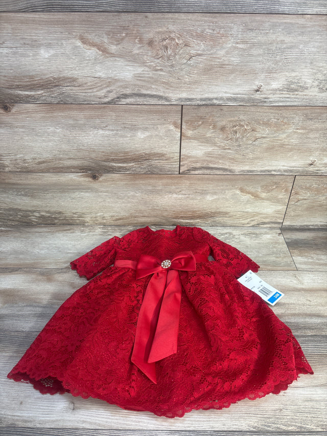 Flat-lay of Rare Editions red toddler lace dress with long sleeves, satin bow and rhinestone brooch on wood floor