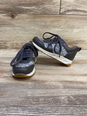 Three-quarter view of Angulus toddler glitter sneakers in grey showing glitter panels and laces with wood floor background