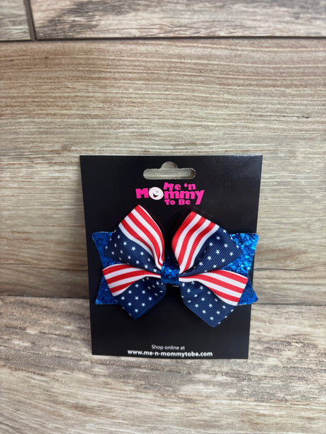 Front view of Fourth of July hair bow showing flag ribbon and blue glitter backing on black card with wood background