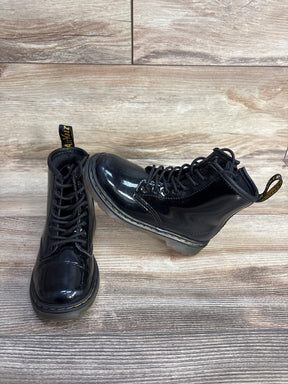 Pair of shiny black combat boots with yellow stitching on wooden floor background