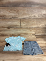 Top-down view of Volcom toddler two-piece set showcasing a light-blue palm-tree short-sleeve shirt and stonewashed jean shorts on wood floor