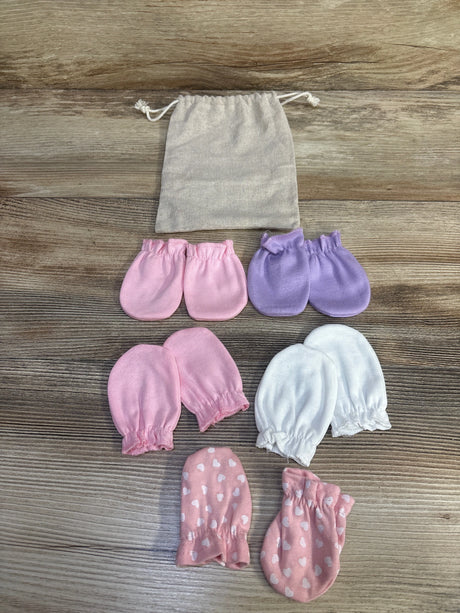 Top-down view of five pairs of baby mittens (pink, lavender, white, pink hearts) with beige pouch on wood background