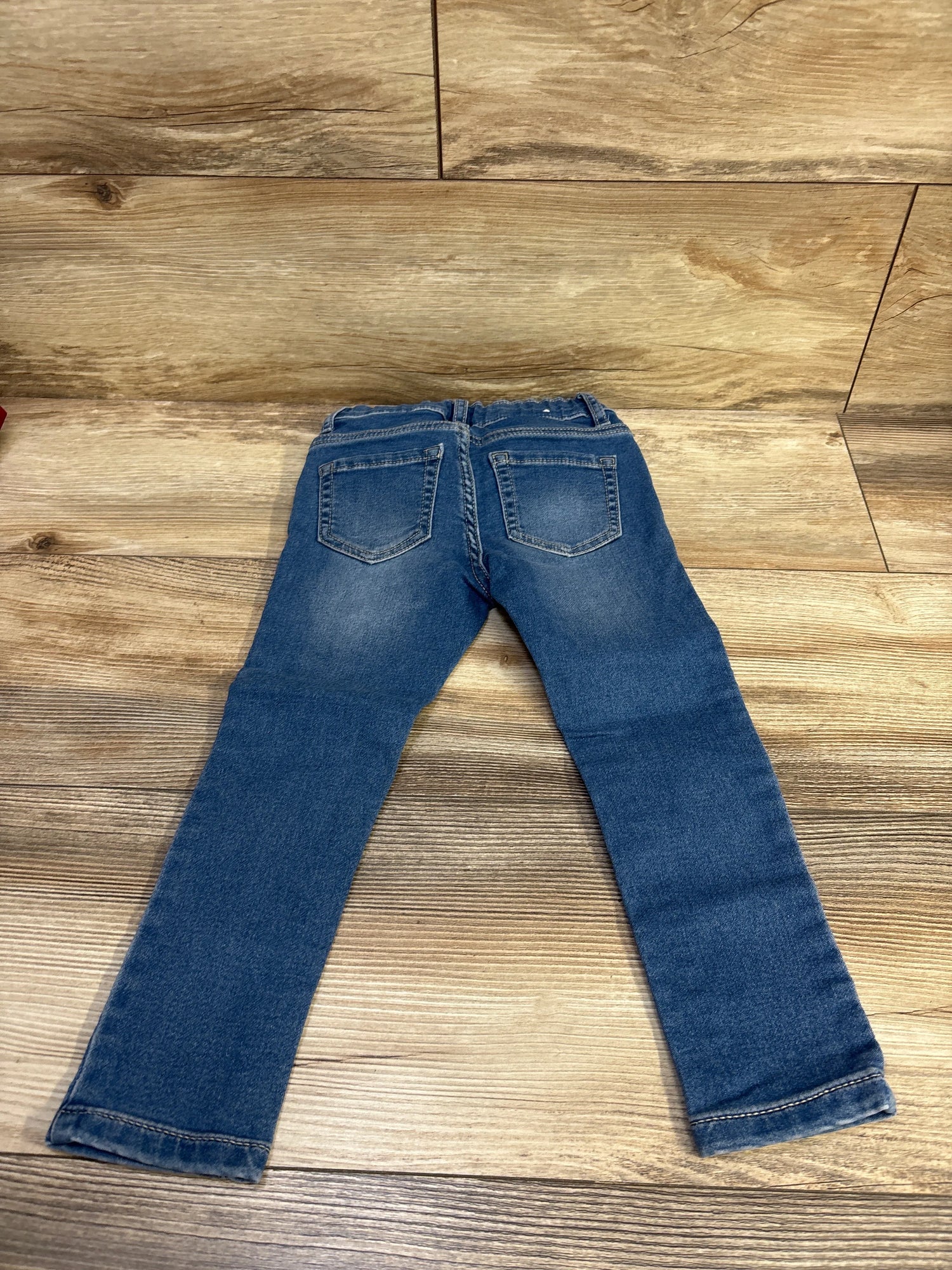 Back view of Children’s Place blue legging jeans in size 4T showcasing stitched back pockets on a wood-grain floor