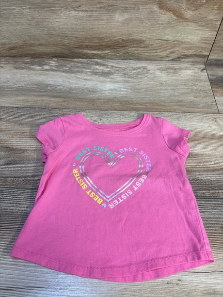 Flat lay of pink Jumping Beans 12M short-sleeve shirt showing metallic heart graphic with 'BEST SISTER' text on wood floor