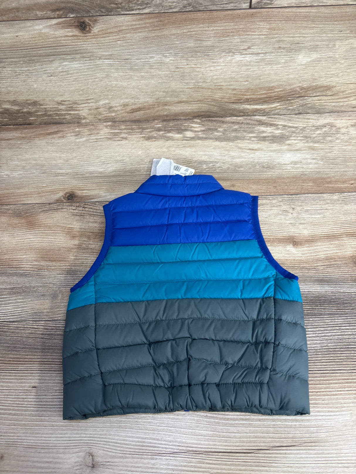 Children's sleeveless puffer vest in blue, teal, and gray colors on wooden surface