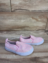 Angled side view of Cat and Jack pink slip-on toddler sneakers showing iridescent glitter uppers and white soles on wood background