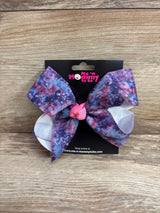 Front view of large hair bow in galaxy purple showing pink center knot and white loops on a black card over wood background