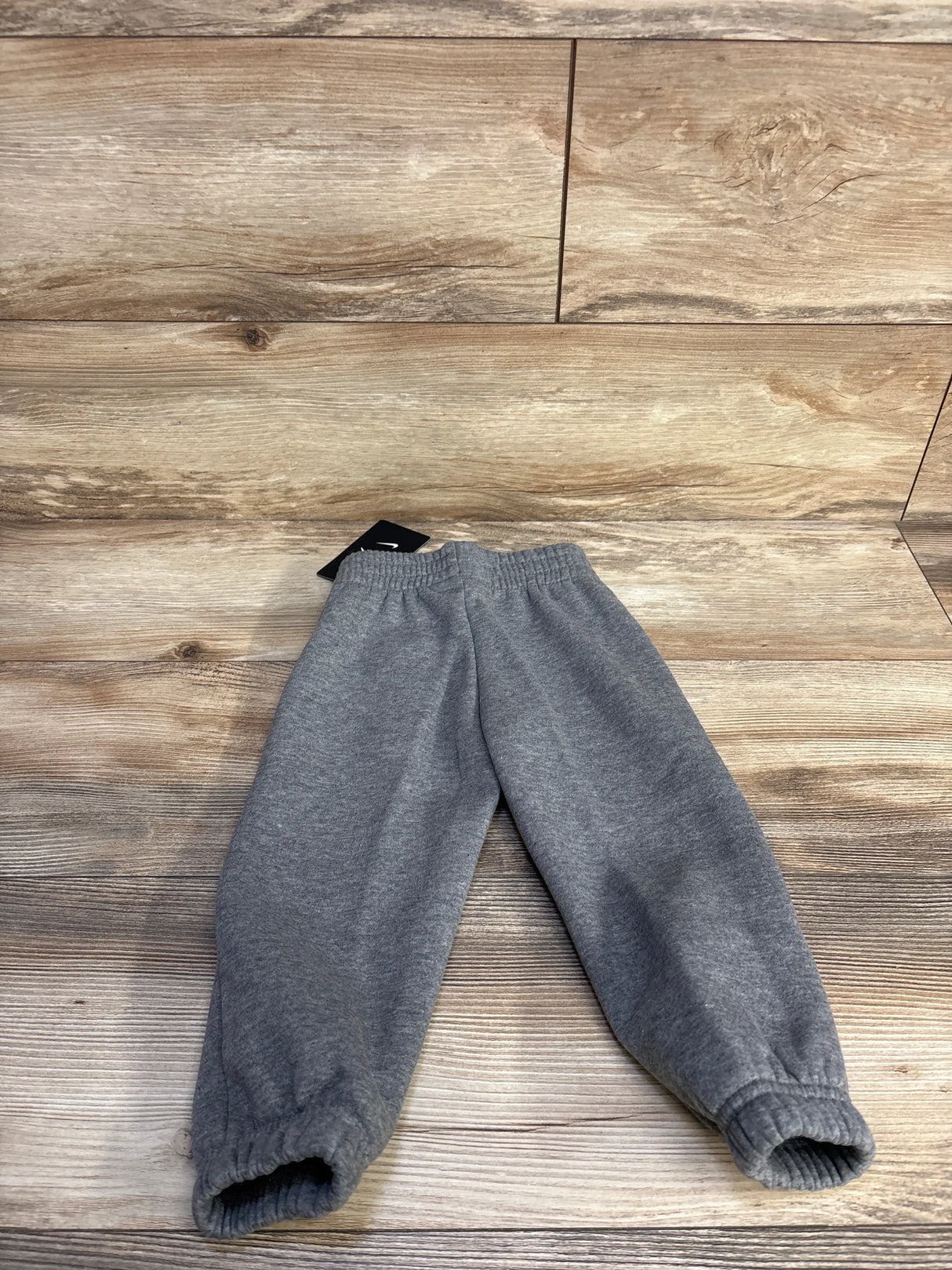 Top-down view of Nike toddler grey joggers showcasing elastic waistband and gathered cuffs on wood floor background