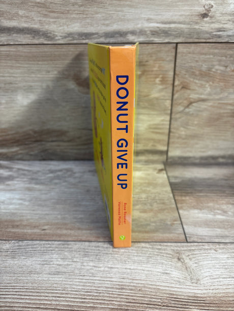 Side view of Donut Give Up board book showing orange spine with blue title text and yellow cover on wooden background