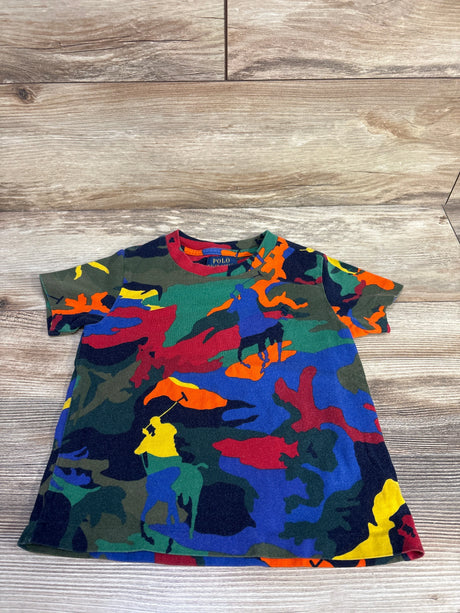 Flat-lay of toddler Polo Ralph Lauren short-sleeve shirt showcasing multicolor camo with polo player silhouettes, size 3T on light wood floor