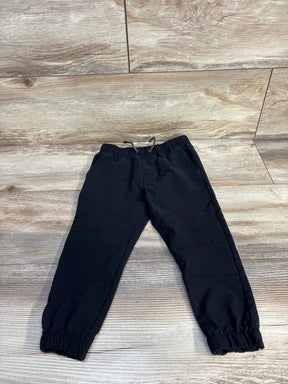 Black kids jogger pants with elastic waist and cuffs, laid on wood floor