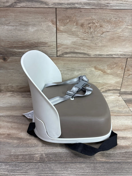Front three-quarter view of the Oxo Tot Perch Booster Seat in taupe showcasing its padded seat and safety harness with a wood-look floor background