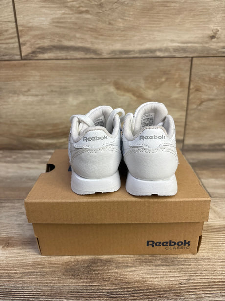 Rear view of white Reebok Classic Leather infant sneakers showing heel Reebok logo on a shoebox with wood background