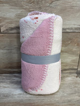 Rolled view of Cloud Island unicorn baby blanket in pink and cream with scalloped stitched edge and gray ribbon on wood background