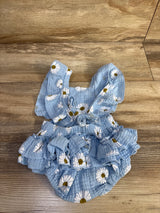 Flat lay of blue gauze baby bubble romper with white daisy print, ruffled straps and ruffled skirt on wood floor