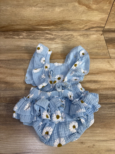 Flat lay of blue gauze baby bubble romper with white daisy print, ruffled straps and ruffled skirt on wood floor