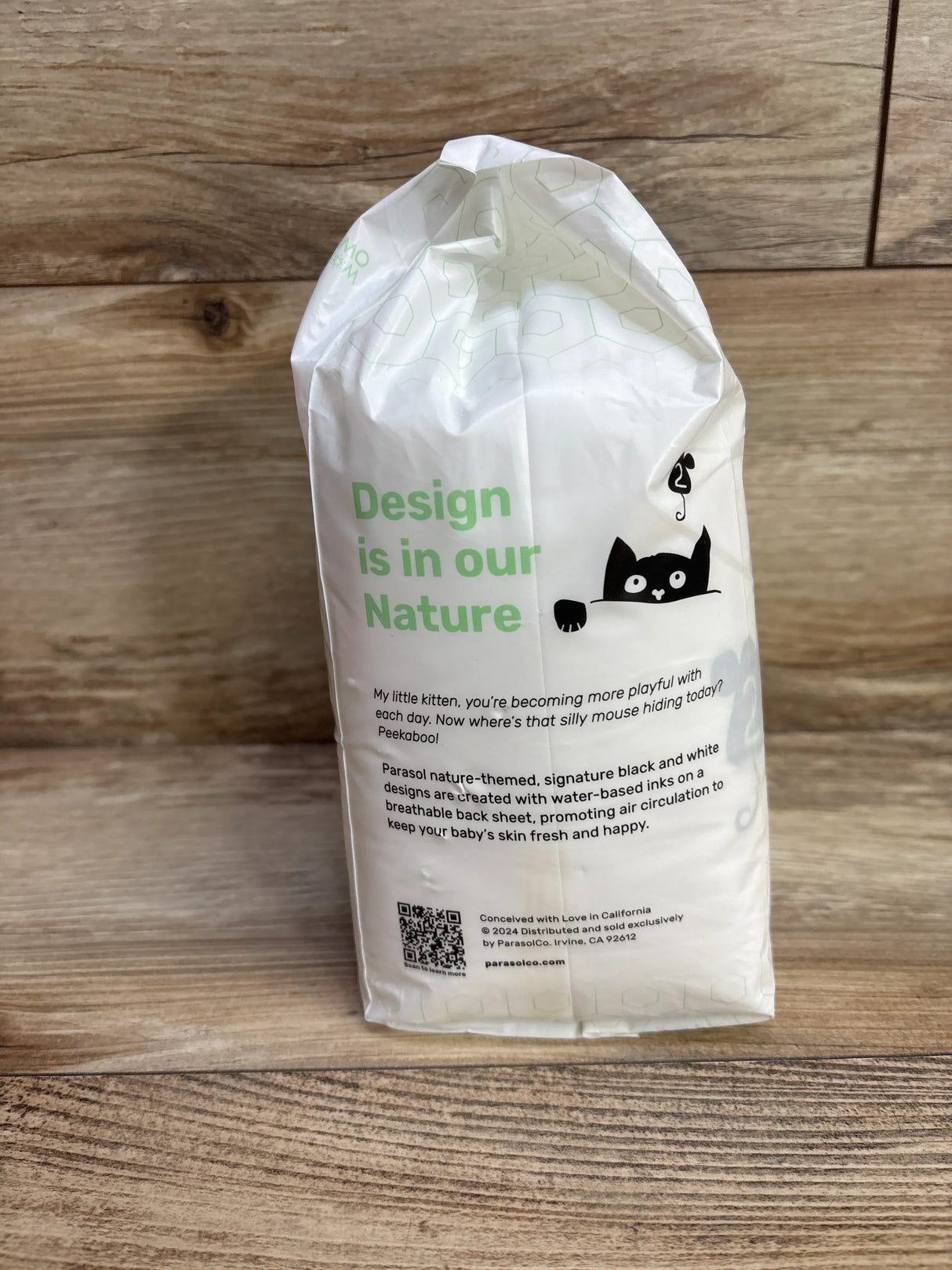Front of Parasol Clear + Dry Bye Bye Rash! diaper pack (size 2, 12ct) showing green 'Design is in our Nature' text and black cat illustration on wood background