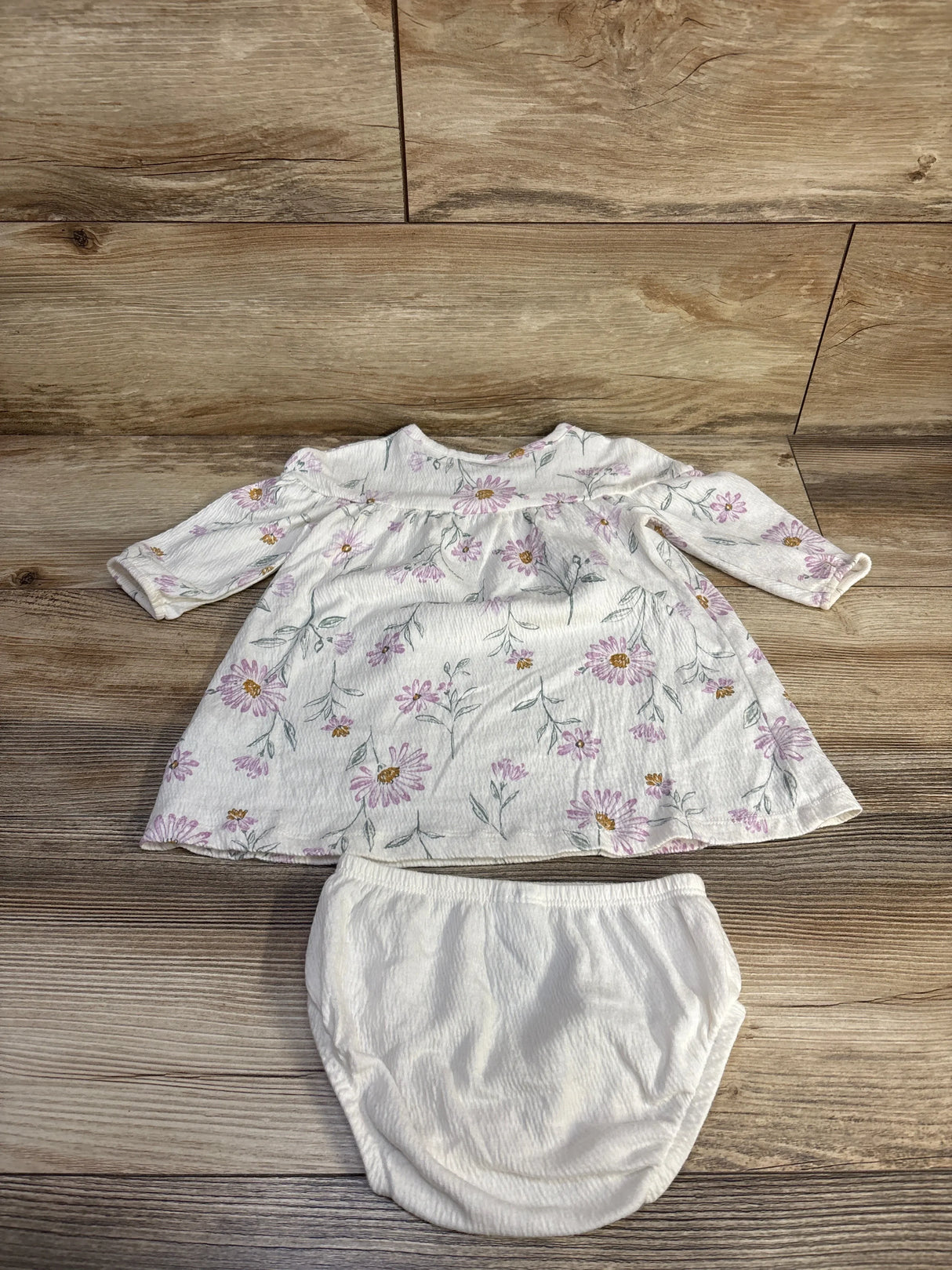 Top-down view of Carter's 2-piece white henley dress with pink floral print and matching white bloomers on wood background