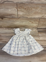 Flat lay of ivory smocked muslin puff-sleeve baby dress with smocked bodice, blue check and red floral print on wood