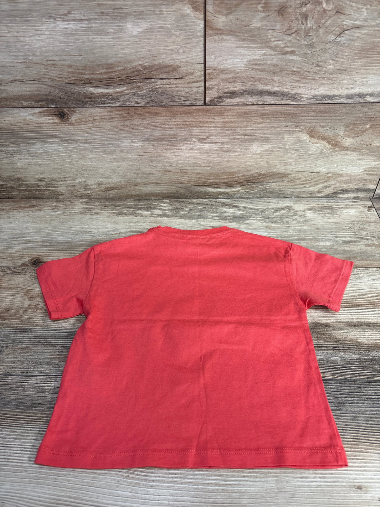Back view of plain coral short sleeve kids t-shirt on wooden floor at children's resale store