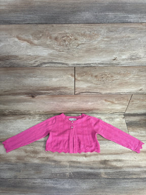 Pink knitted baby cardigan with scalloped hem and pearl buttons on wooden floor