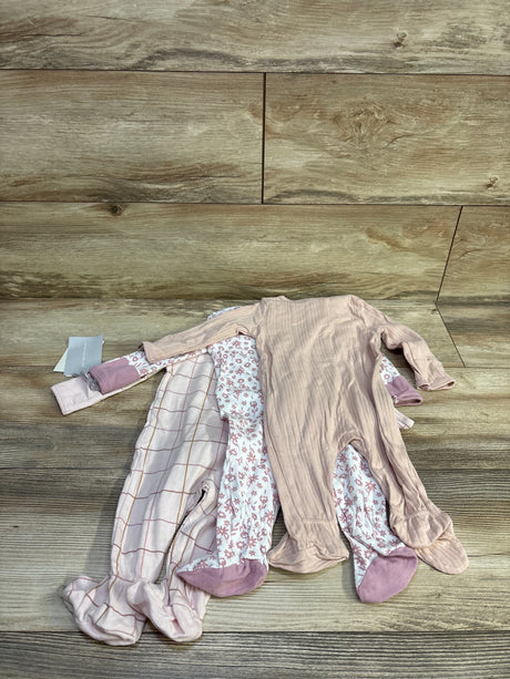 Flat lay of Cloud Island 3-pack footed sleepers showing ribbed pink, floral, and pale checked prints on wood background