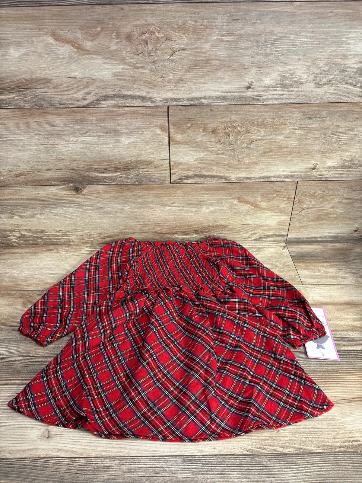 Red plaid kids dress with ruffled waist, laid on wood floor, resale clothing