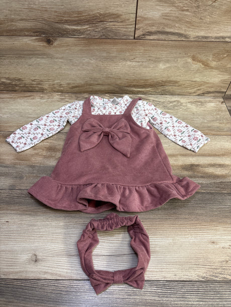 Top view of Daisy Fuentes 3-piece outfit with white floral bodysuit, mauve skirtall with bow, and matching headband on wood