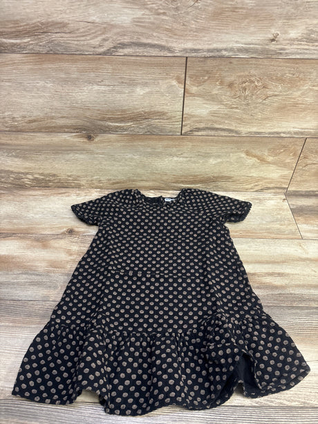 Front view of Old Navy black swing dress in size 5T with tan circular pattern, short sleeves, and ruffled hem on wood flooring