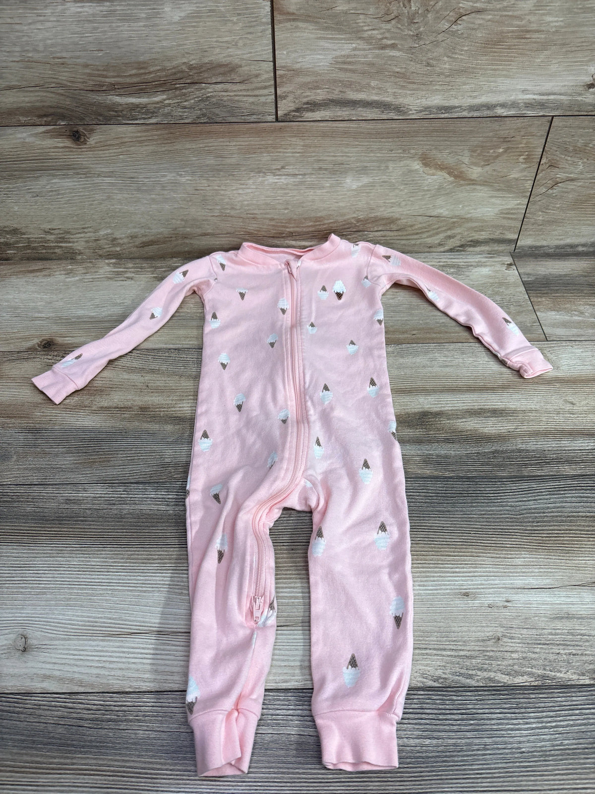 Front view of Pekkle pink sleeper in size 18 months showcasing ice cream cone print and front zipper on a wood-grain background