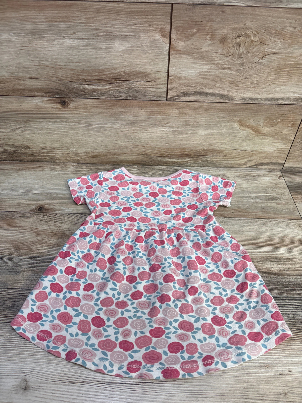 Flat lay of girls' pink floral dress size 4T showing short sleeves, gathered waist, and rose print on wood floor background
