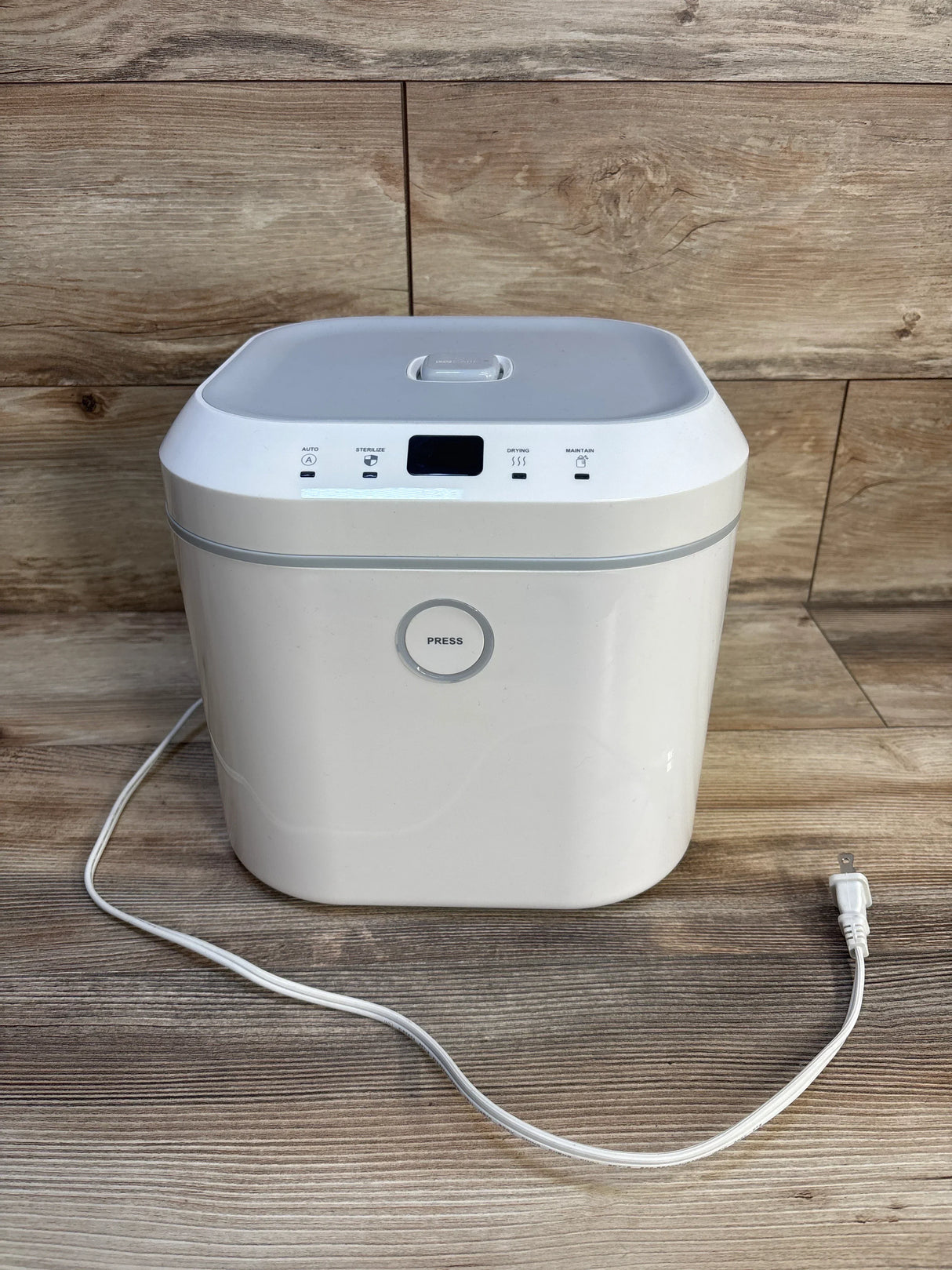White baby bottle sterilizer with lid and power cord on wood floor background