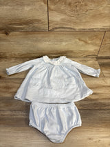 White baby outfit with long sleeves, ruffled collar, and matching bloomers on wooden floor
