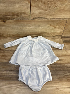 White baby outfit with long sleeves, ruffled collar, and matching bloomers on wooden floor