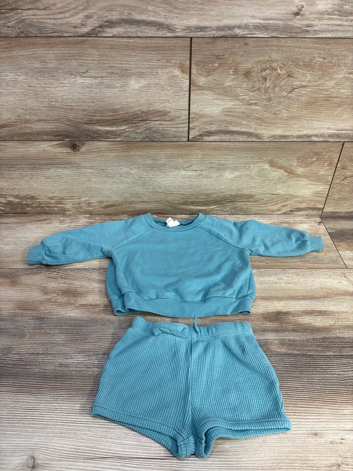 Flat lay of teal baby long-sleeve shirt and waffle-knit shorts showing waffle texture and drawstring waist on wood background