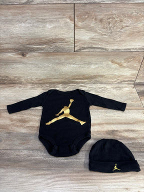 Black baby bodysuit and hat set with gold basketball logo on wood background