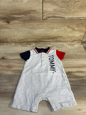 Front flat lay of Tommy Hilfiger romper showing light grey body, red and navy sleeves, vertical TOMMY text and snap crotch on wood floor