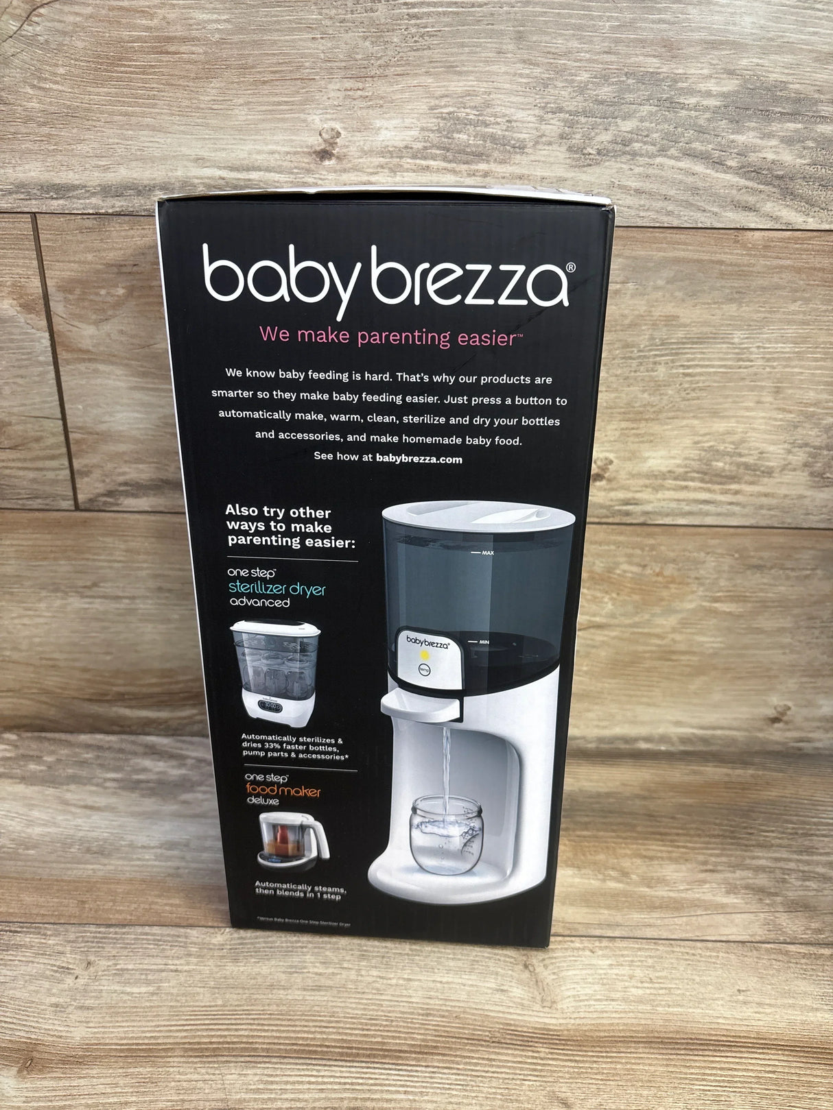 Front view of Baby Brezza Instant Baby Bottle Warmer box showing babybrezza logo and dispenser spout with wood plank background