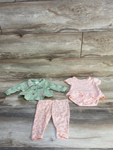 Flat-lay of Nanette Baby 3-piece set: embroidered green jacket, pink ruffle bodysuit, and floral leggings on wood background