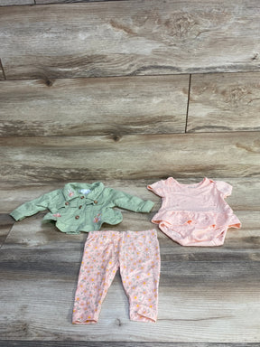 Flat-lay of Nanette Baby 3-piece set: embroidered green jacket, pink ruffle bodysuit, and floral leggings on wood background