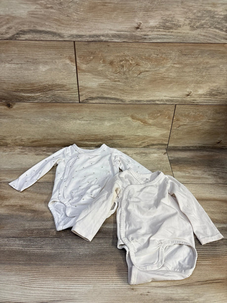 Top-down view of two white H&M organic wrapover baby bodysuits showing long sleeves and front snap closures on a wood floor